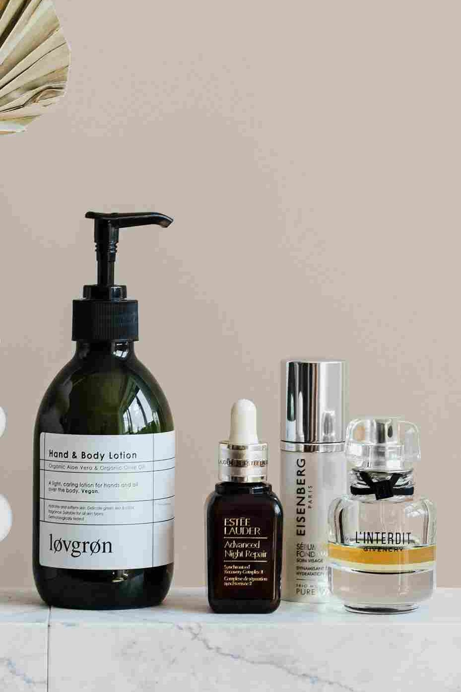 A minimalist skincare setup featuring a hand and body lotion, a face serum, a moisturizer, and a perfume bottle on a marble surface with a decorative vase. How to Choose Face Serum for Dry Skin – identifying the best hydrating products for dry skin care. | womenluxlife.com