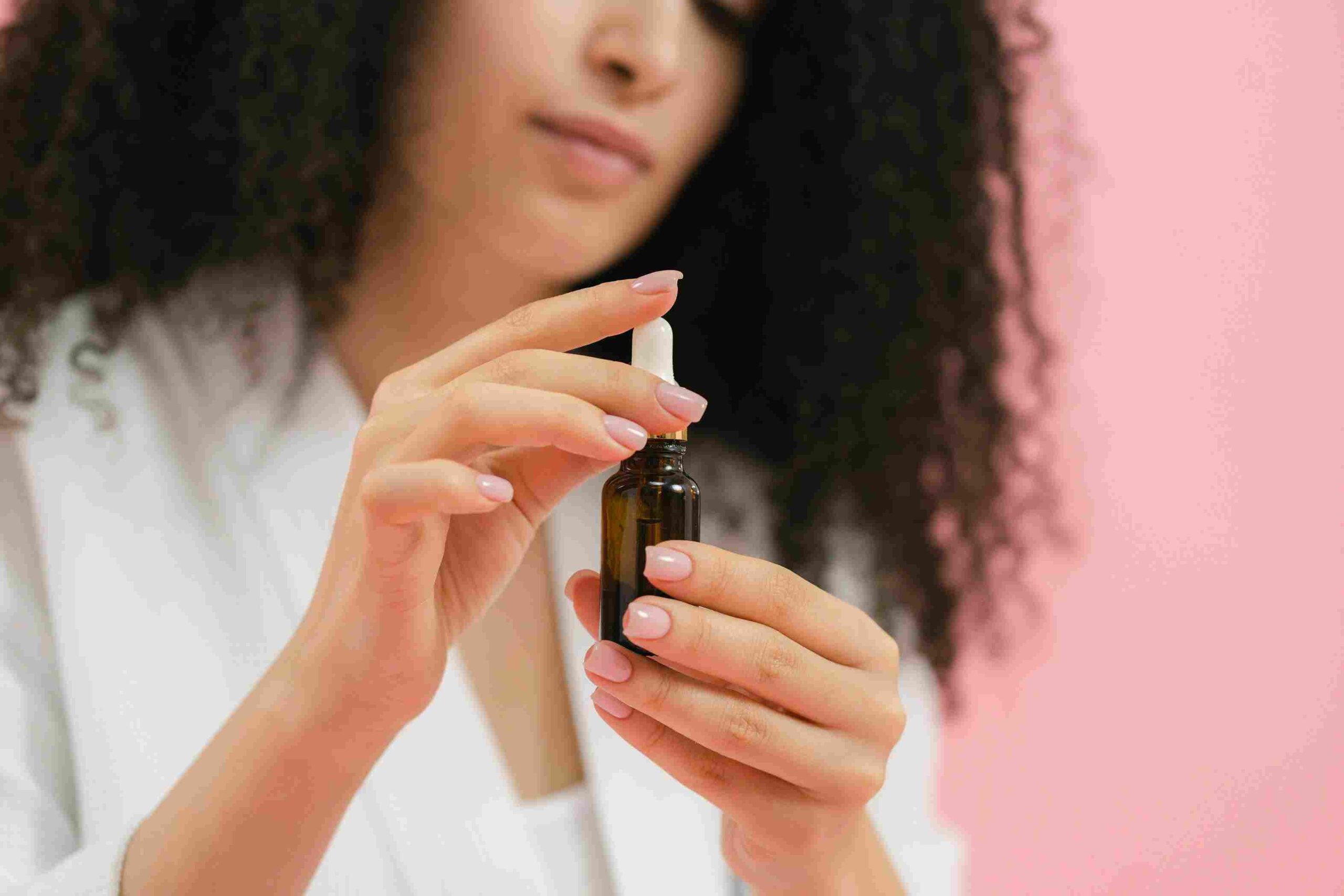 A woman with curly hair in a white robe holding a dropper bottle, applying face serum. The image represents skincare and hydration. How to Choose Face Serum for Dry Skin – selecting the right serum for nourishment and moisture.