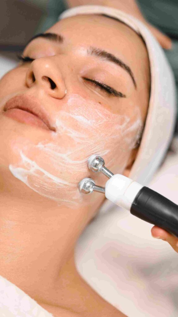 A close-up of a woman receiving a skincare treatment, where a cream is applied to her face and a beauty tool is used for facial massage. The image illustrates the effectiveness of creams for dry skin in the context of "Serum vs. Cream for Dry Skin. | womenluxlife.com