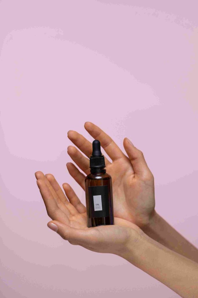 A close-up of a hand holding a brown glass bottle of face serum against a pink background. What Happens If I Stop Using Face Serum – will my skin become dry and dull? | womenluxlife.com