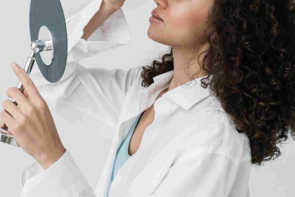 A woman applying face serum while looking into a mirror. What Happens If I Stop Using Face Serum – will my skin lose its glow and hydration? | womenluxlife.com