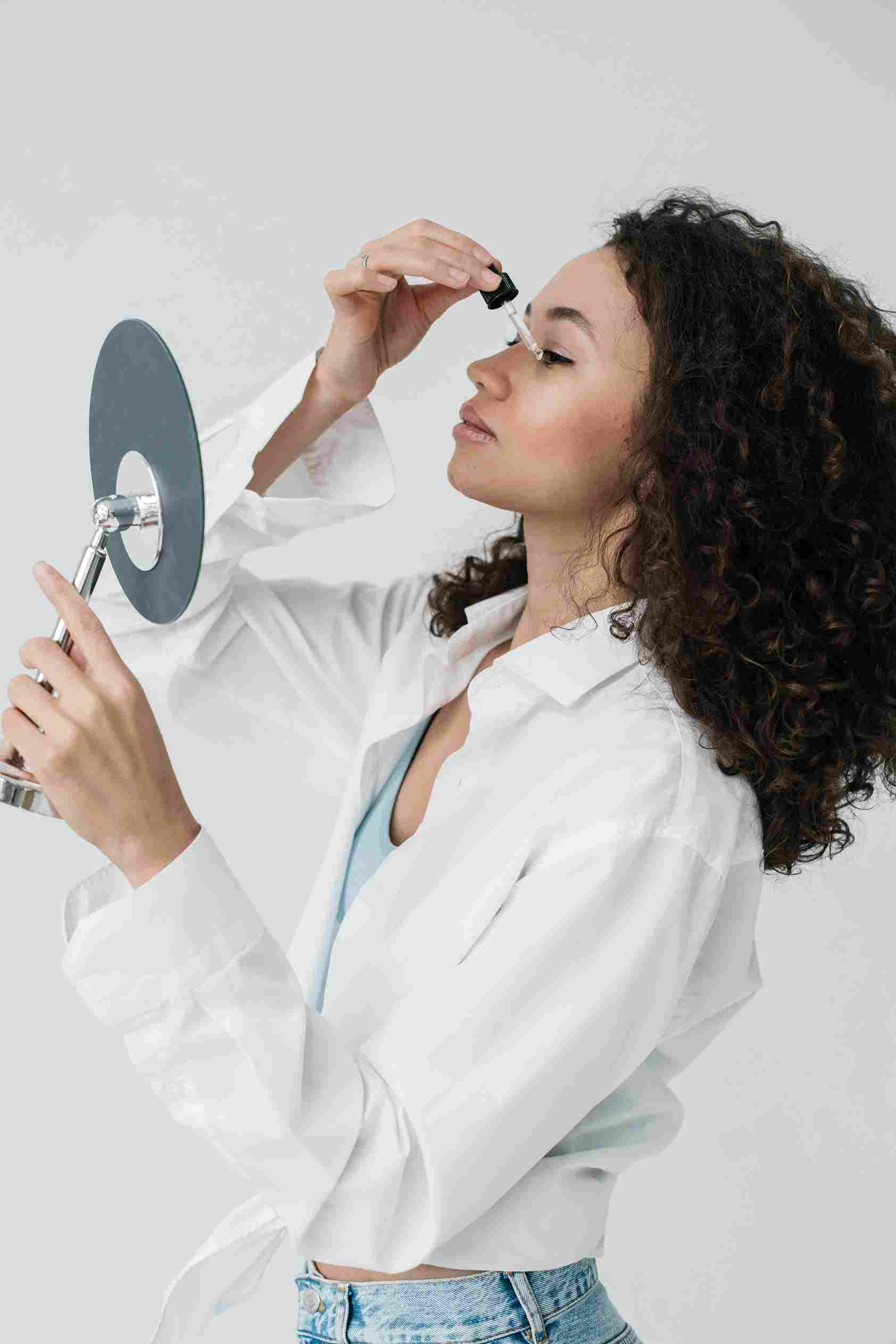 A woman applying face serum while looking into a mirror. What Happens If I Stop Using Face Serum – will my skin lose its glow and hydration? | womenluxlife.com